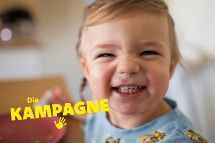 Ein Kleinkind grinst in die Kamera. Auf dem Bild ist der Schriftzug "Die Kampagne" abgebildet.