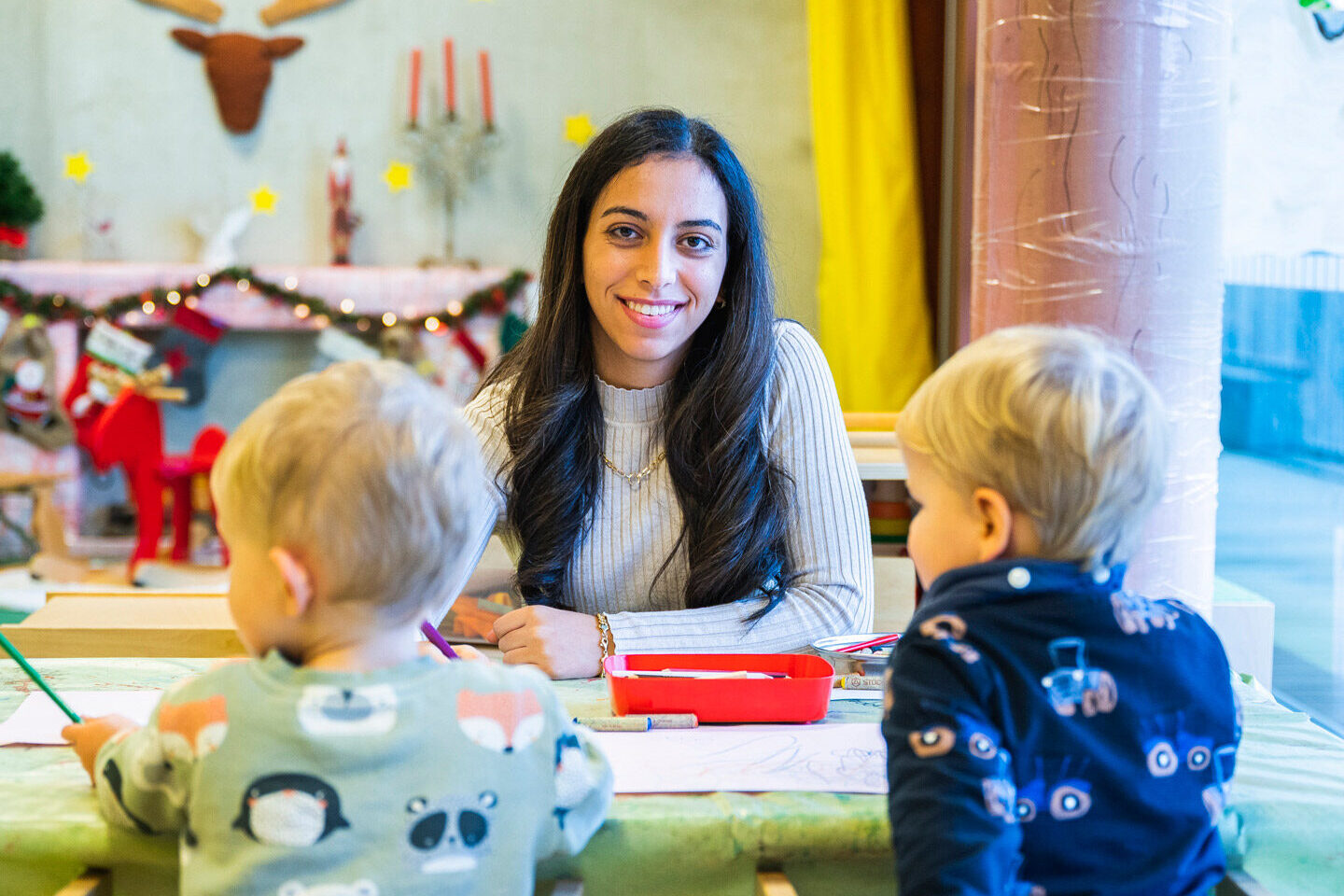 Eine junge Frau malt mit zwei kleinen Kindern zusammen an einem Maltisch.